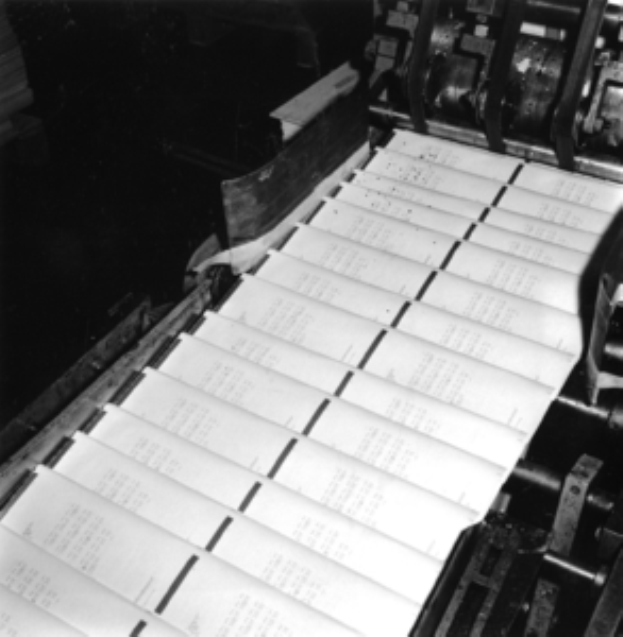 Ein Schwarz-Weiß-Foto von einer Druckerpresse mit mehreren Zeitungen darauf.