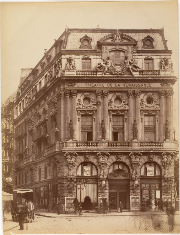 Schwarz-weiß-Fotografie des Théâtre de la Renaissance in Paris mit einer Fassade mit Fenstern, Säulen, Bögen und Skulpturen, mit ein paar Menschen und Fahrzeugen auf der Straße davor und dem Himmel im Hintergrund.