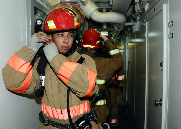 Feuerwehrleute in Uniform während einer Übung in einem Raum stehend, mit Rohren und Gegenständen im Hintergrund.