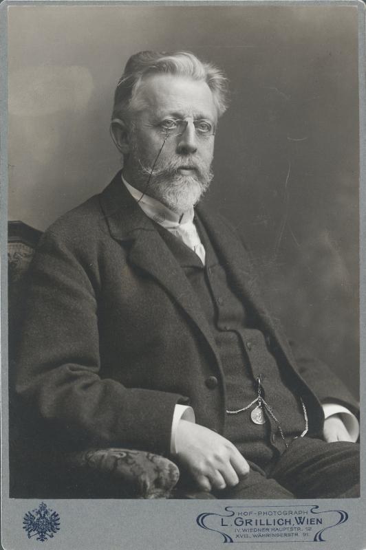 Schwarzes und weißes Porträt eines bärtigen Mannes mit Brille, der in einem Stuhl sitzt, beschriftet mit "L. Grillich Wien, der Gründer der deutschen Revolution."