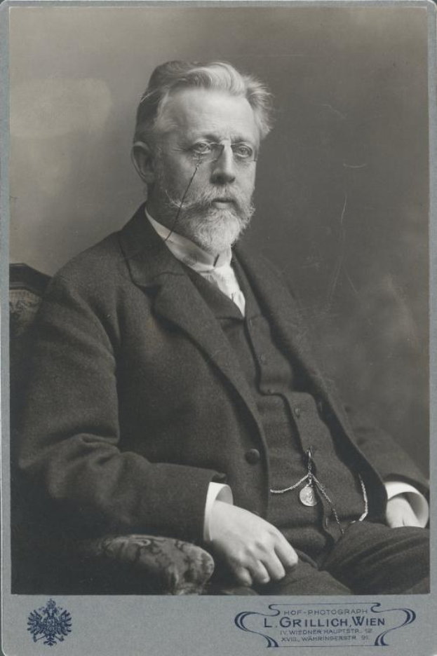 Schwarzes und weißes Porträt eines bärtigen Mannes mit Brille, der in einem Stuhl sitzt, beschriftet mit "L. Grillich Wien, der Gründer der deutschen Revolution."