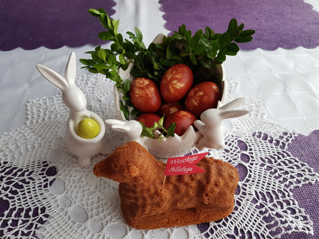 Ein mit einer Decke drapierter Tisch trägt eine Schüssel voller bunter Oster-Eier mit Osterhasen-Figuren darauf.
