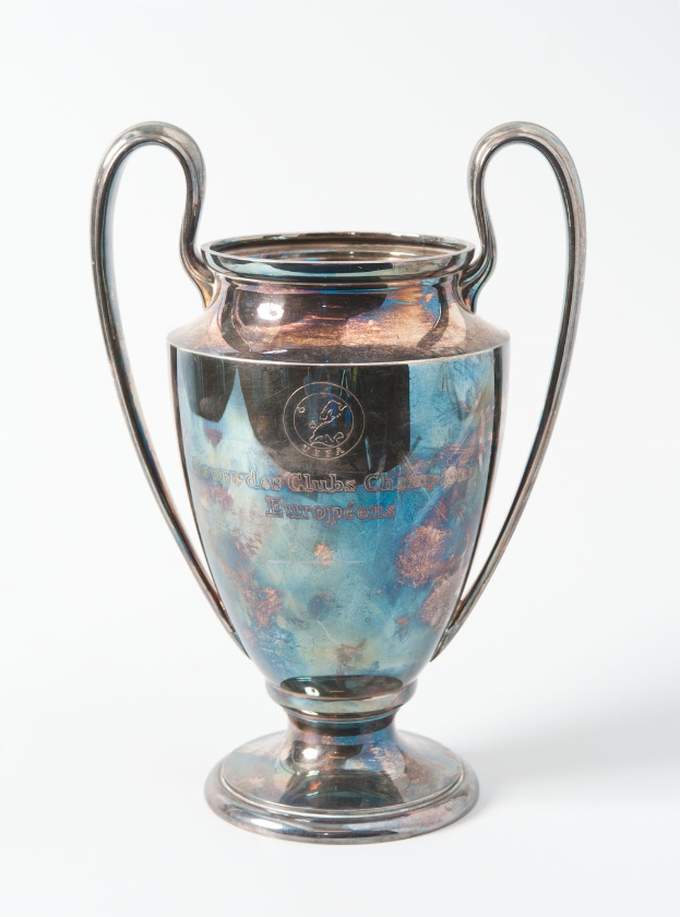 Der UEFA-Champions-League-Pokal, ein stählerner Pokal mit zwei Griffen und einem blauen und silbernen Farbschema, mit der Inschrift "UEFA Champions League" auf einem weißen Hintergrund.