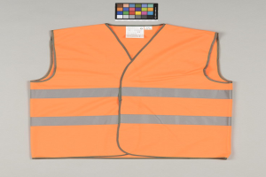 Leuchtend orangefarbene Sicherheitsweste mit Reflektoren und einem Anhänger auf einem grauen Hintergrund.