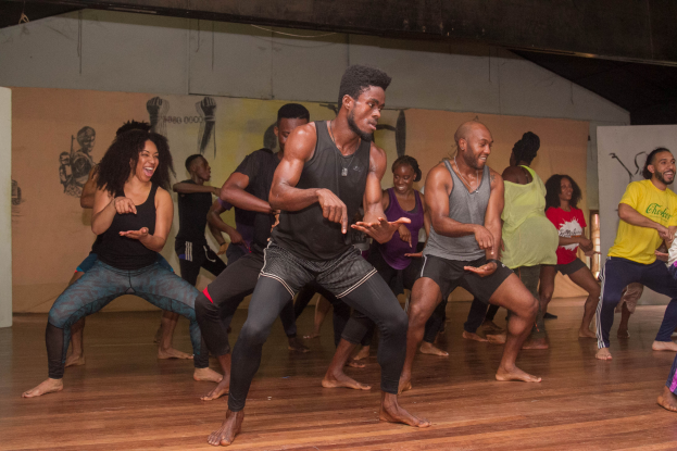 Eine Gruppe von Menschen tanzt in einem Choreografie-Kurs an der Universität Chicago, mit einer Wand voller Bilder im Hintergrund und einer Decke über ihnen.