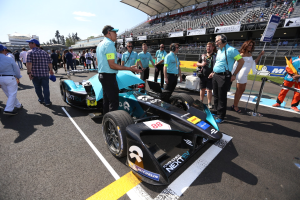Eine Gruppe von Menschen feiert um ein Formel-E-Rennfahrzeug auf einer Rennstrecke, mit einem Stadion im Hintergrund, das von Zuschauern gefüllt ist.