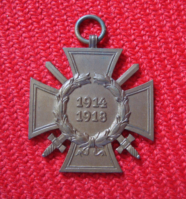 Rotes Tuch mit einer silbernen Medaille, die einen Lorbeerkranz zeigt, in der Mitte des Tuchs mit eingravierter Schrift.