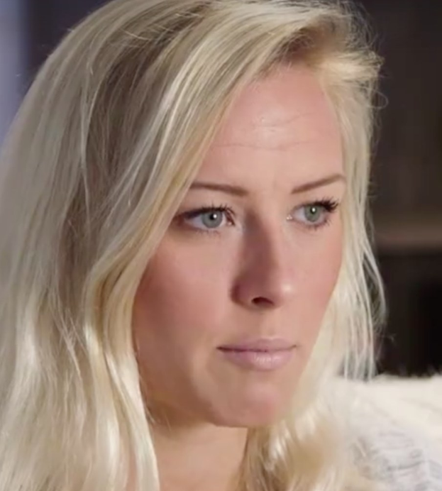 Blonde Frau mit blauen Augen im Vordergrund, unscharfer Hintergrund, wirkt besorgt.