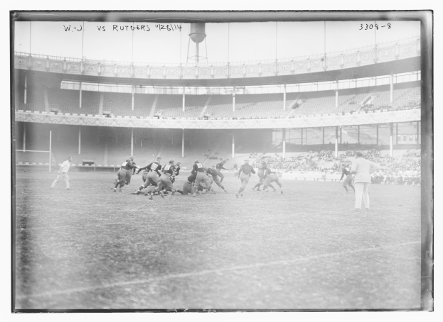 Schwarzes und weißes Foto eines Fußballspiels im Gange mit Spielern auf dem Feld und Zuschauern in den Rängen, das Text an der Spitze enthält.