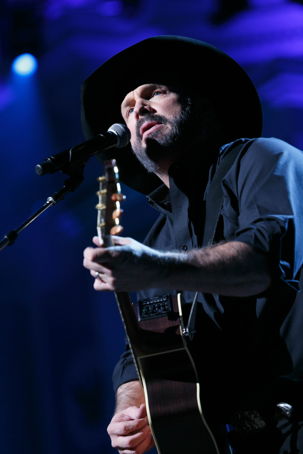 Garth Brooks trägt ein schwarzes Hemd und eine schwarze Mütze und performs auf der Bühne beim CMA Music Festival in Nashville, Tennessee, spielt eine Gitarre und singt in ein Mikrofon.