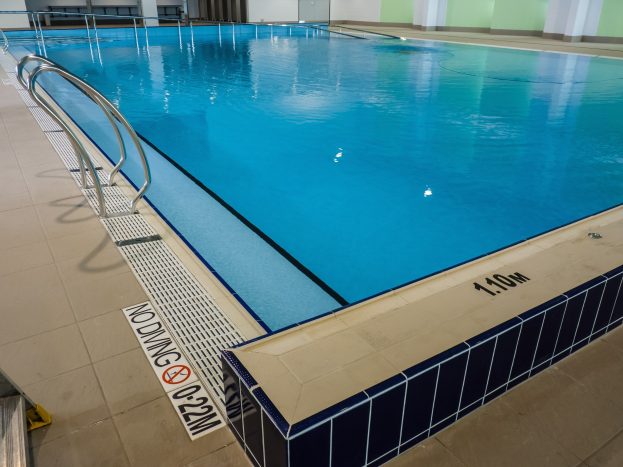 Indoor-Schwimmbad mit Fliesenboden, Metallstreben, einem Schild, einer Tür und Deckenlampen in einem großen Gebäude.