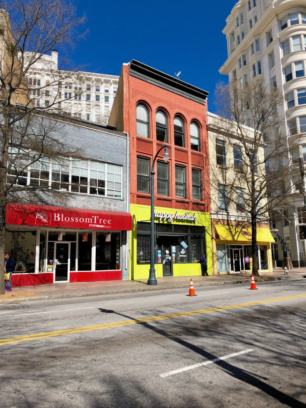 Eine Straße in der Innenstadt von Portland mit hohen Gebäuden, Kraftfahrzeugen, Verkehrskegeln, Fußgängern, Straßenlaternen und Bäumen unter einem bewölkten Himmel.