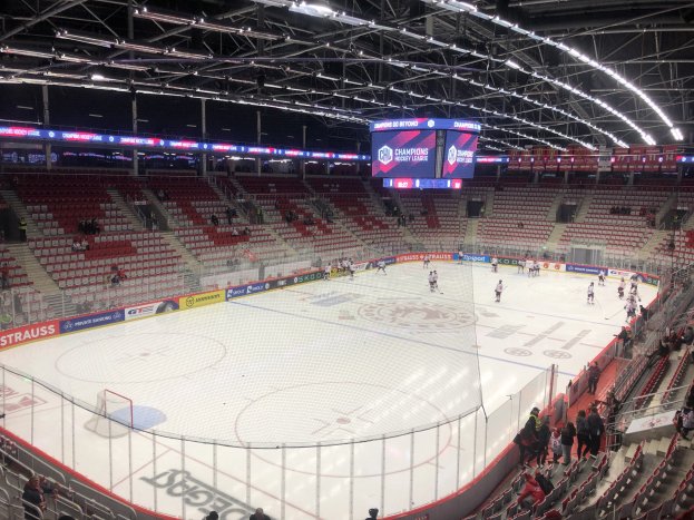 Eishockeyspiel in einer großen Arena mit Zuschauern, ein Eisring umgeben von einem Zaun, ein Display mit "St. Louis Blues vs Detroit Red Wings", Metallrahmen, eine Decke mit Deckenlampen und eine Decke.