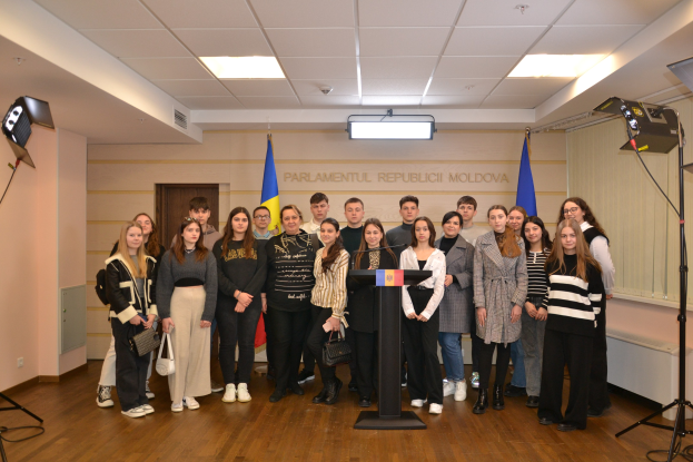 Gruppe von Menschen auf einem Podium mit Mikrofonen, umgeben von moldauischen Flaggen, einer Wand mit "Moldova Youth Congress 2018", einer Tür, Deckenlampen und Scheinwerfern.