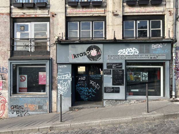 Ein Gebäude mit Fenstern, Geländern, Türen, Texttafeln, Plakaten, Pfosten und Graffiti an der Seite, das sich über einer Straße befindet.