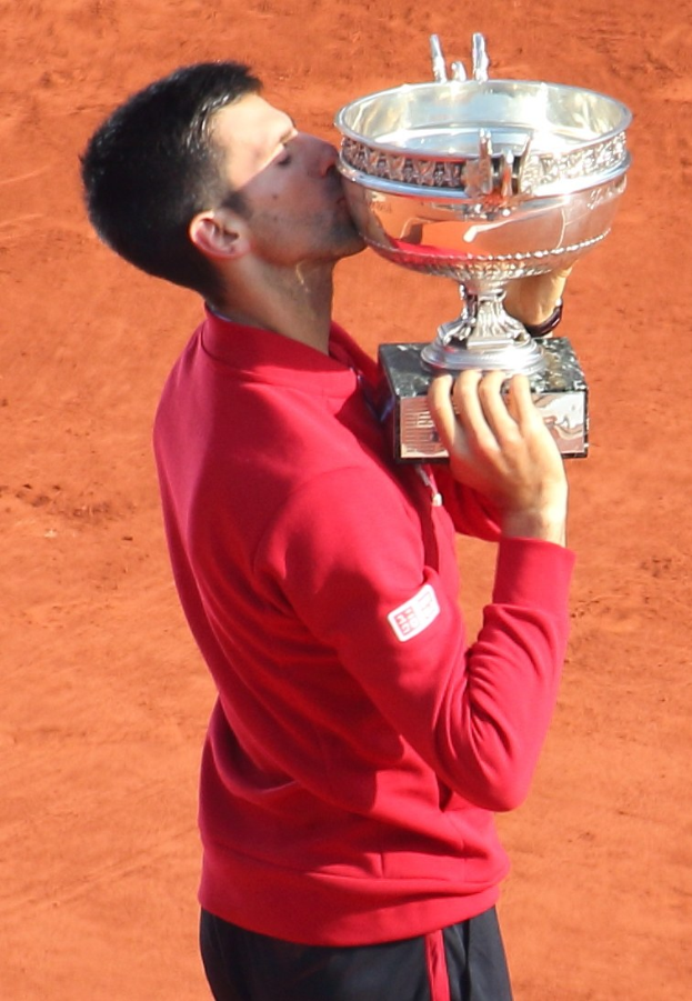 Novak Djokovic hält den French Open-Pokal nach Sieg gegen Rafael Nadal im Herrensingelfinale in den Händen und küsst ihn mit triumphierendem Gesichtsausdruck.