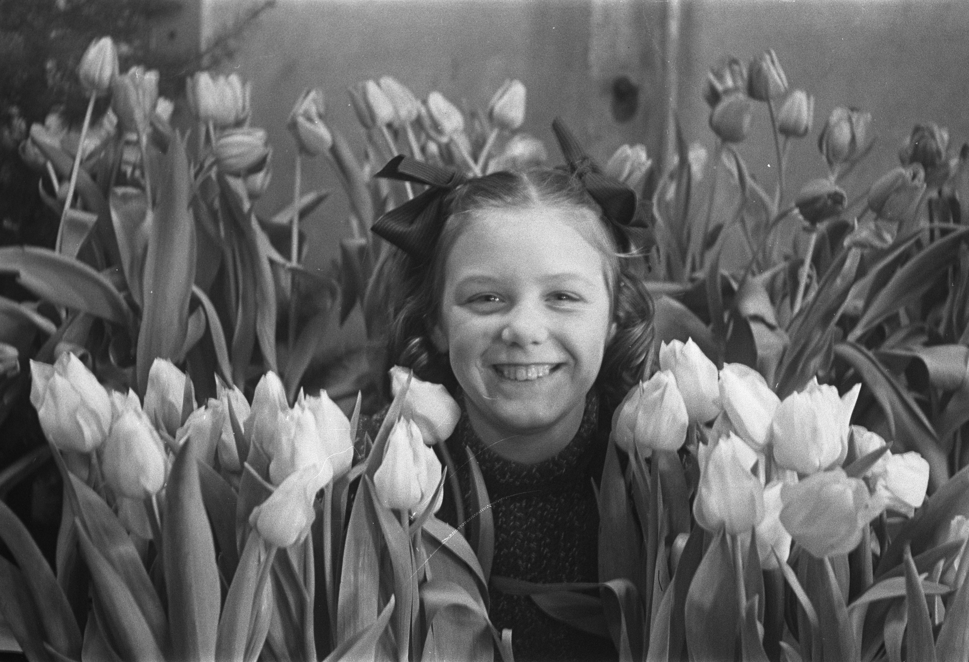Schwarz-weiß-Foto eines jungen Mädchens, das in einem Feld voller leuchtender Tulpen lächelt.