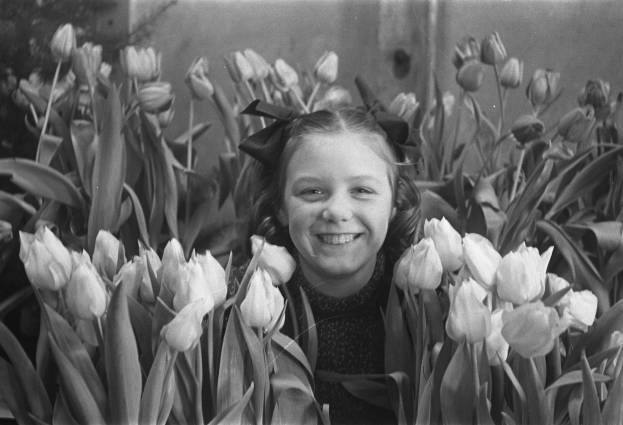 Schwarz-weiß-Foto eines jungen Mädchens, das in einem Feld voller leuchtender Tulpen lächelt.