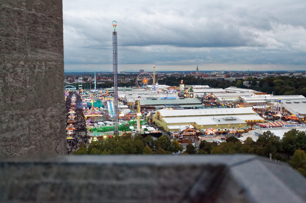 Freizeitpark-Ansicht von oben, mit einer Wand, Bäumen, Gebäuden, Fahrgeschäften und Pfählen im Vordergrund und einem bewölkten Himmel im Hintergrund.