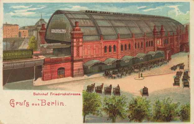 Schwarz-weiß-Postkarte eines alten Berliner Bahnhofs mit einem Gebäude, Bäumen, Wagen, Menschen, einer Brücke und einem bewölkten Himmel, mit Text unten.