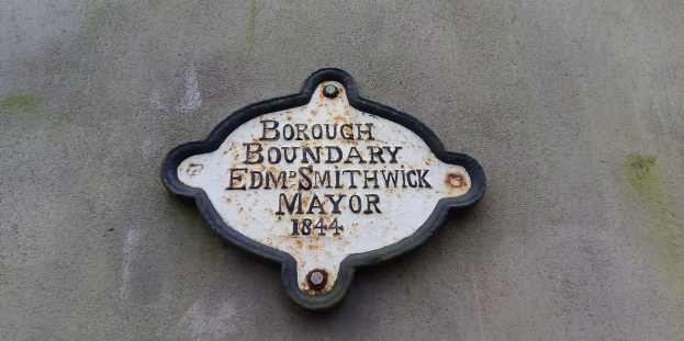 Metallplakette an einer Gebäudeseite mit schwarzem Hintergrund und weißer, fetter, zentrierter Schrift, die "Stadtgrenze Edm Smithwick Bürgermeister" liest.