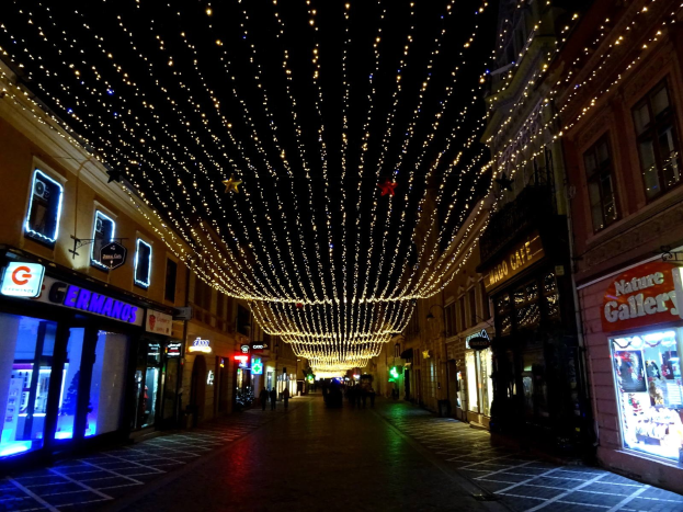 Eine festlich geschmückte Stadtstraße bei Nacht mit Weihnachtsbeleuchtung, gesäumt von Gebäuden und einigen Passanten.