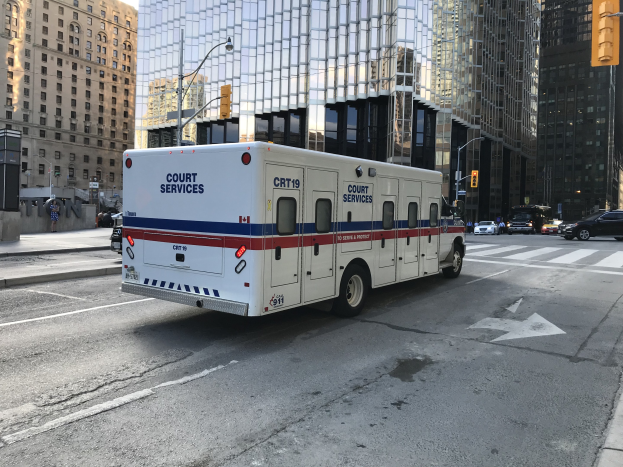 Ambulanz auf einer Stadtstra├če mit hohen Geb├Ąuden, Stra├čenm├Âbeln und Passanten, unter einem sichtbaren Himmel.