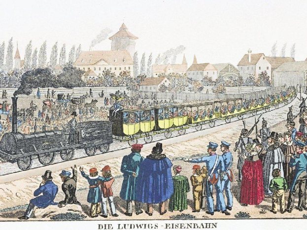 Gruppe von Menschen um ein stehendes Zug auf Schienen mit Gebäuden und Bäumen im Hintergrund, Bezug nehmend auf "Ludwigs-Eisenbahn, die erste Bahnstation in Deutschland" unten.