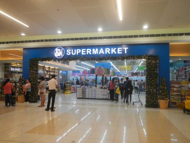 Gruppe von Menschen vor einem Supermarkt mit Einkaufstägern, Taschen, Blumentopf, Regalen, Schildern und Deckenleuchten.