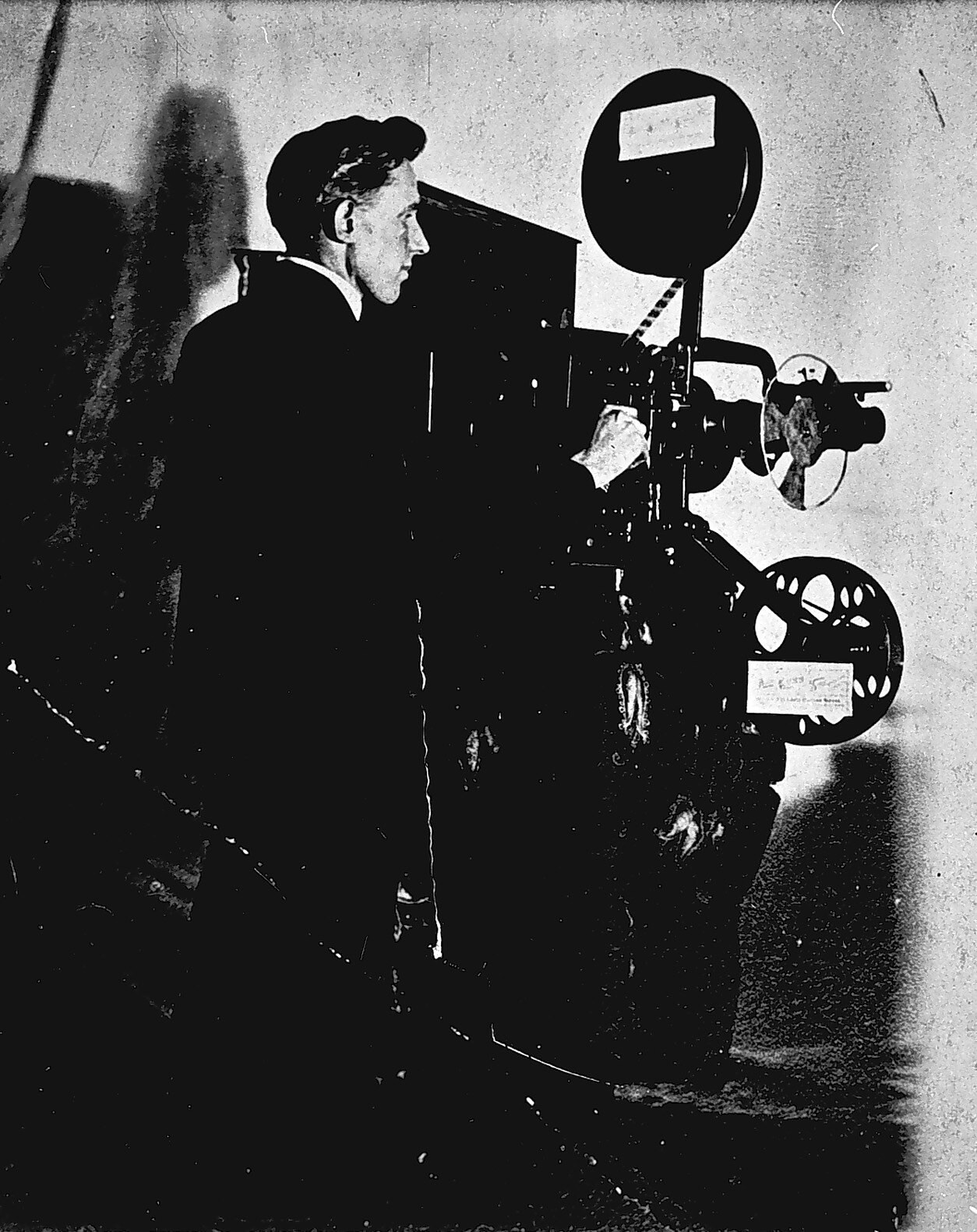 Ein Mann in einem Anzug steht neben einem alten Filmprojektor und sieht konzentriert aus.