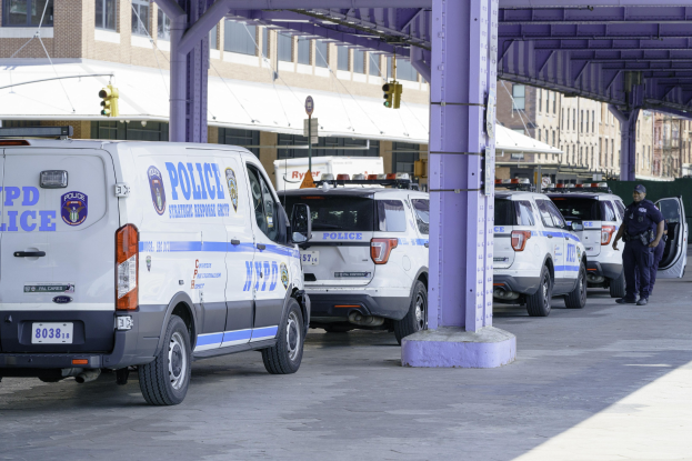 Polizeifahrzeuge entlang einer Stadtstraße geparkt, mit einer Person in der Nähe, Hintergrund enthält Gebäude, Pfosten, Verkehrsampeln und eine Brücke.