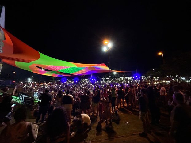 Eine große Menschenmenge steht vor einem hell erleuchteten Zelt bei Nacht während des 2018er Kunstfestivals, mit bunten Lichtern und Pfählen, die die Szene beleuchten, einem Gebäude links und dem Nachthimmel im Hintergrund.