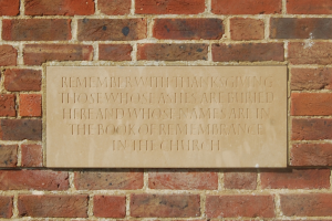 Eine Backsteinmauer mit einer Plakette, auf der steht: "Erinnere dich mit Dankbarkeit an diejenigen, deren Asche hier begraben ist und deren Namen im Buch der Erinnerung in der Kirche stehen."