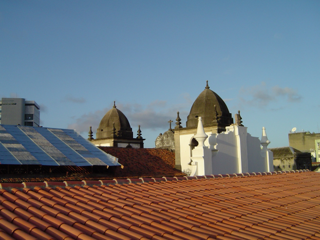 Stadtpanorama mit Gebäuden im Vordergrund, einem klaren blauen Himmel im Hintergrund und Solarpanelen auf einem Dach.