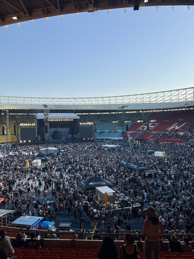 Große Menschenmenge sitzt und steht in einer Halle mit Zelten, Geländern und Deckenbeleuchtung während eines Konzerts in der O2 Arena in London.