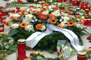 Gedenkstätte in Berlin mit Blumen und Kerzen vor einer Wand.