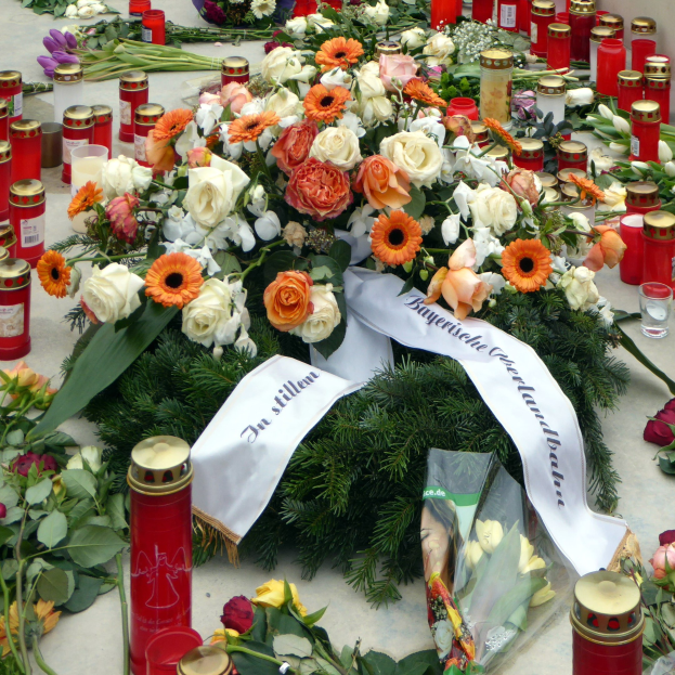 Gedenkstätte in Berlin mit Blumen und Kerzen vor einer Wand.