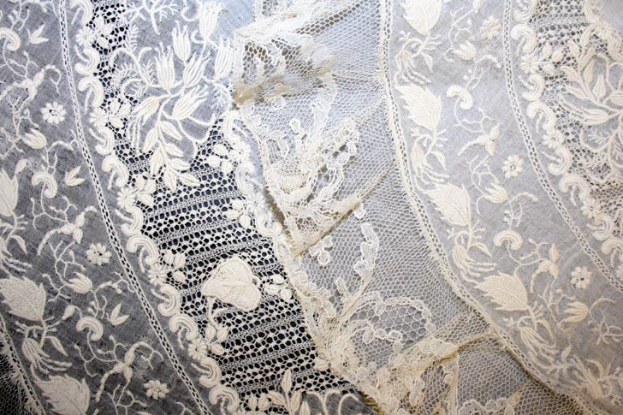 Nahaufnahme eines weißen Hochzeitskleids mit feiner Spitze und zarten, verschiedenen Mustern auf einem leichten, luftigen Stoff.