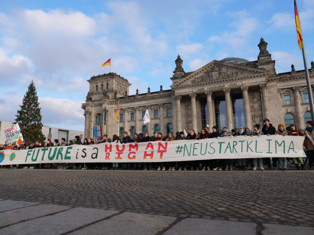 Eine Gruppe von Menschen vor dem Reichstaggebäude in Berlin, die eine Fahne mit der Aufschrift 'Zukunft ist ein Menschenrecht.' halten.