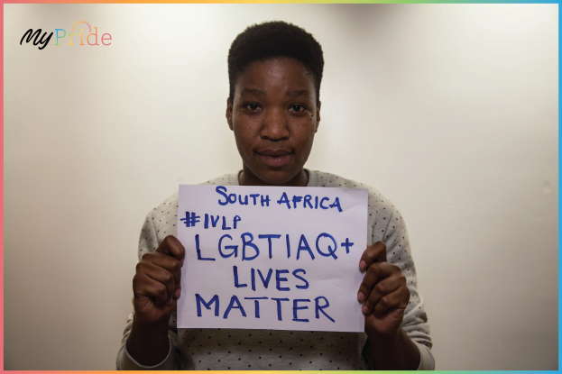 Eine Frau in einem weißen Hemd hält ein Schild hoch, auf dem "LGBTQ+ Lives Matter" steht, vor einer Wand. Ihr entschlossener Gesichtsausdruck drückt Solidarität mit der LGBTQ+-Gemeinde aus.