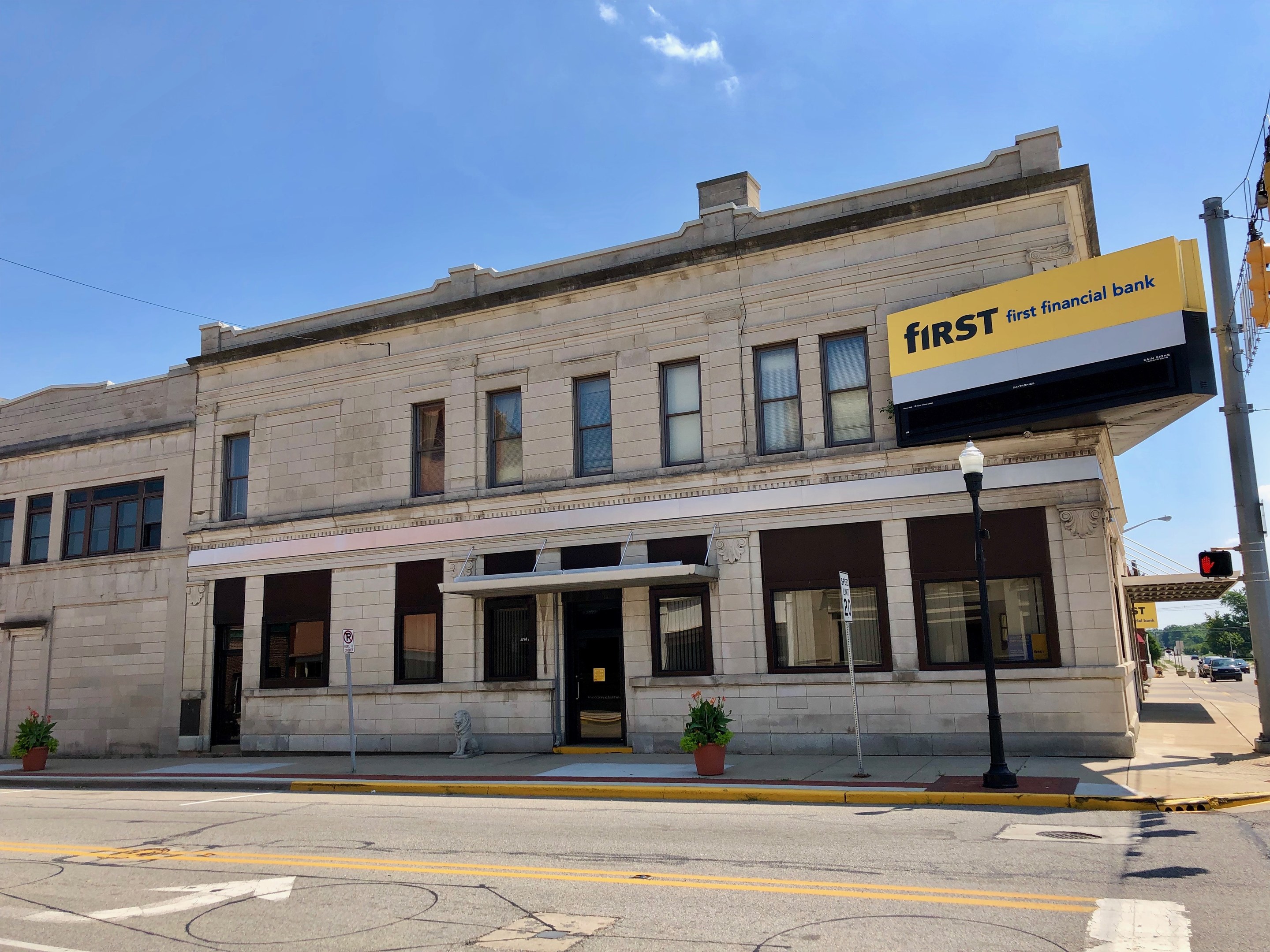 Großes Gebäude mit einer "First Financial Bank"-Plakette, umgeben von Straßeninfrastruktur, Fahrzeugen, Grünflächen und einem bewölkten Himmel.