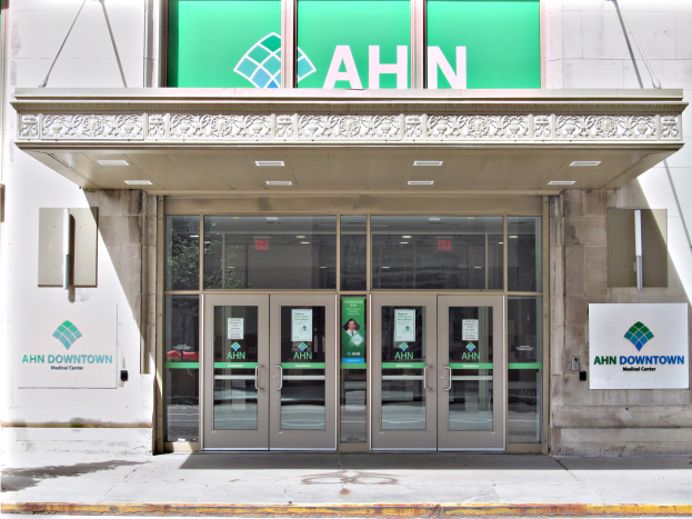 Eintritt zum Ahn Downtown Medical Center mit einem grün-weißen "ahn downtown"-Schild, Glastüren mit Plakaten, Wandtafeln und Deckenleuchten.