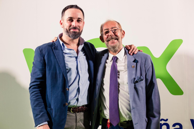 Zwei Männer in Anzügen lächeln nebeneinander vor einer Wand, wobei der Mann rechts eine Brille trägt und ein Schild im Hintergrund die Aufschrift 'Vodafone und Vodacom kündigen Partnerschaft an' trägt.
