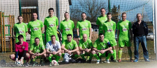 Eine Gruppe von Männern in grünen T-Shirts steht auf einem Fussballfeld, einige hocken, mit einem Ball und einem Torpfosten zu sehen.