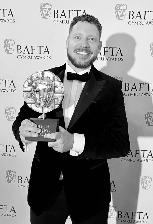 Ein Mann in einem Smoking, der eine BAFTA-Trophäe hält und vor einem Hintergrund mit der Aufschrift "BAFTA Awards 2018" steht.
