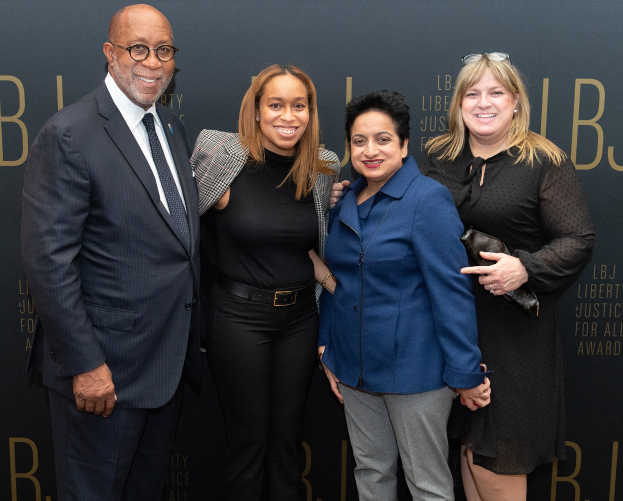 Eine Gruppe von vier Personen auf einem roten Teppich, die lächeln und für ein Foto posieren, mit einem 'Liberty Justice for All Awards'-Schild im Hintergrund.