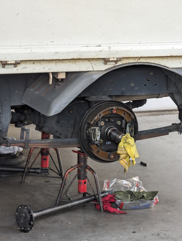 Ein gelber, mit einem Tuch bedeckter Lkw in einer Garage mit Werkzeugen und Gegenständen, die vor ihm auf dem Boden verstreut sind.