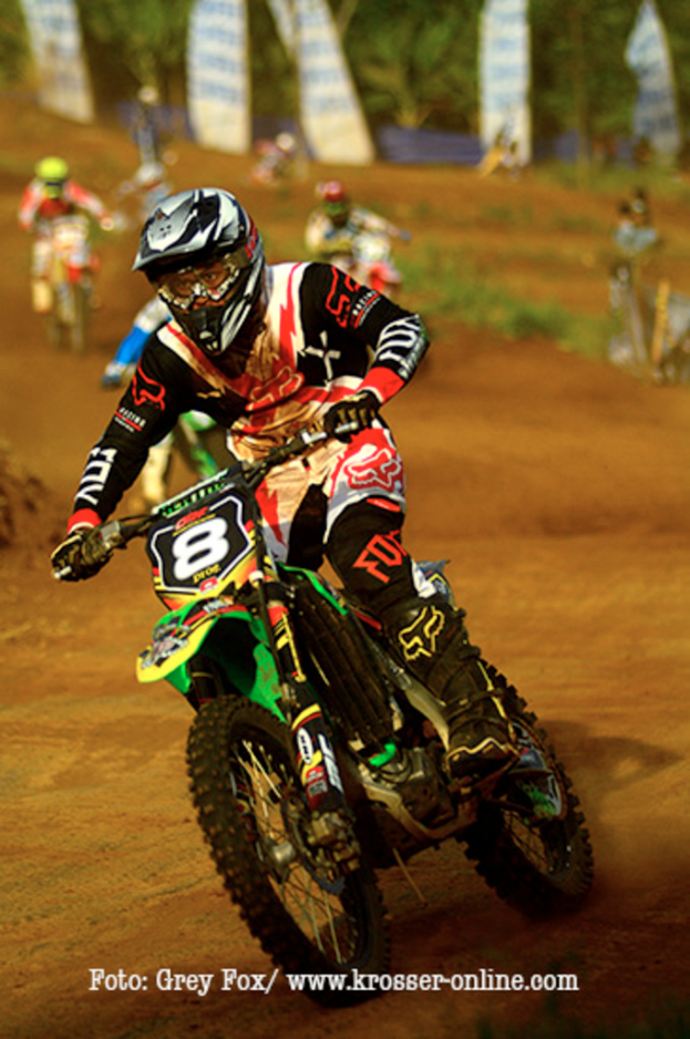 Mehrere Motorradfahrer mit Helmen rasen, mit Text am Bildunterrand.