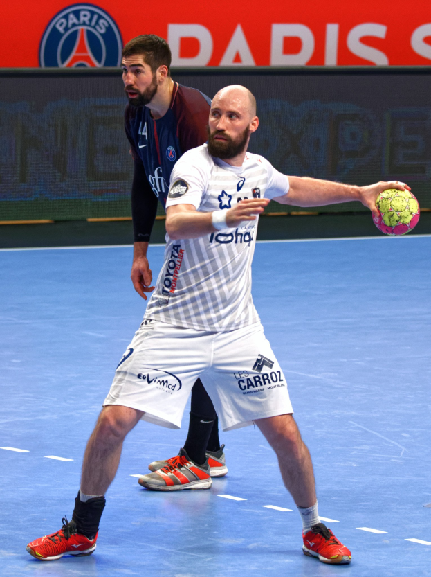 Zwei Männer beim Handballspielen auf einem Feld, einer hält den Ball, im Hintergrund ein Schild mit der Aufschrift "Paris Saint-Germain vs Paris Saint-Germain."