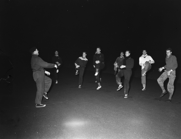 Eine Gruppe von Männern in Schuhen auf einer Bühne in einem Schwarz-Weiß-Setting, das eine Vorstellung suggeriert.